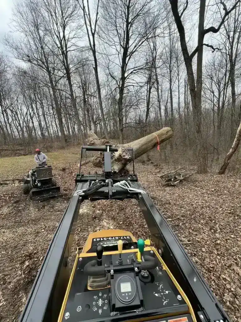 Mini skid steer grabbing logs on a cleared lot in Carmel, IN