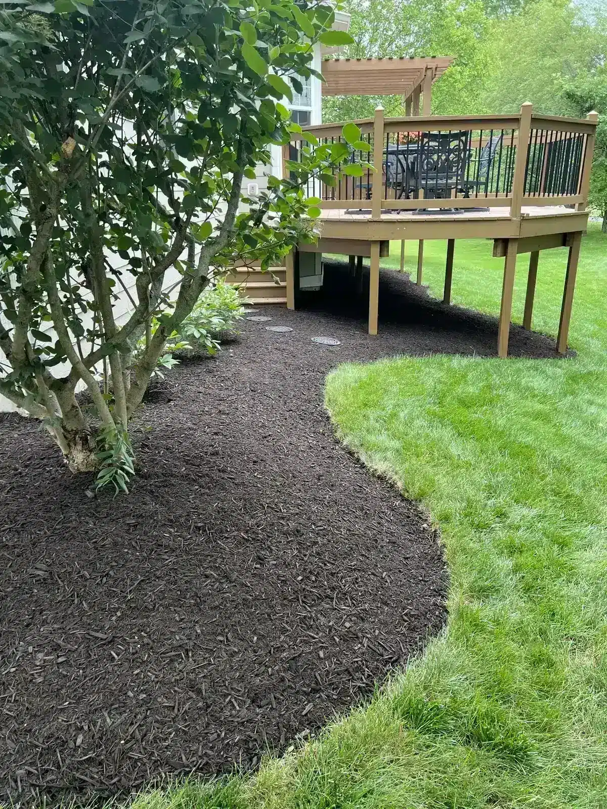 Curved bed edged and mulched under a deck, serving Whitestown, IN