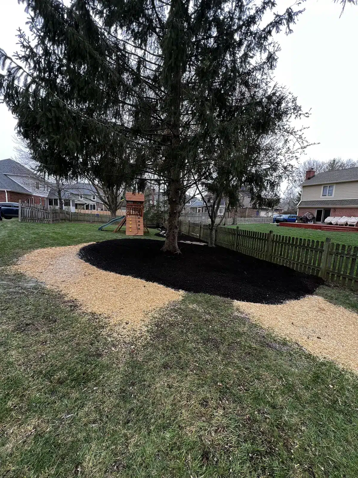 Fresh mulch bed under an evergreen next to a backyard play set, serving Nora, IN